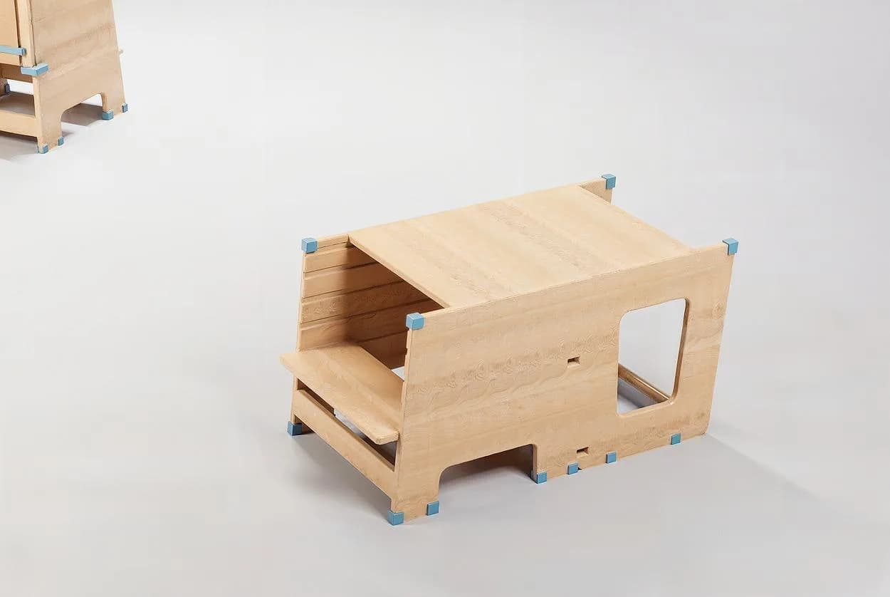 La Torre de Aprendizaje en su configuración de banca y mesa baja, con tablero inclinado a modo de atril y peldaño escalonado, vista de tres cuartos sobre fondo blanco.