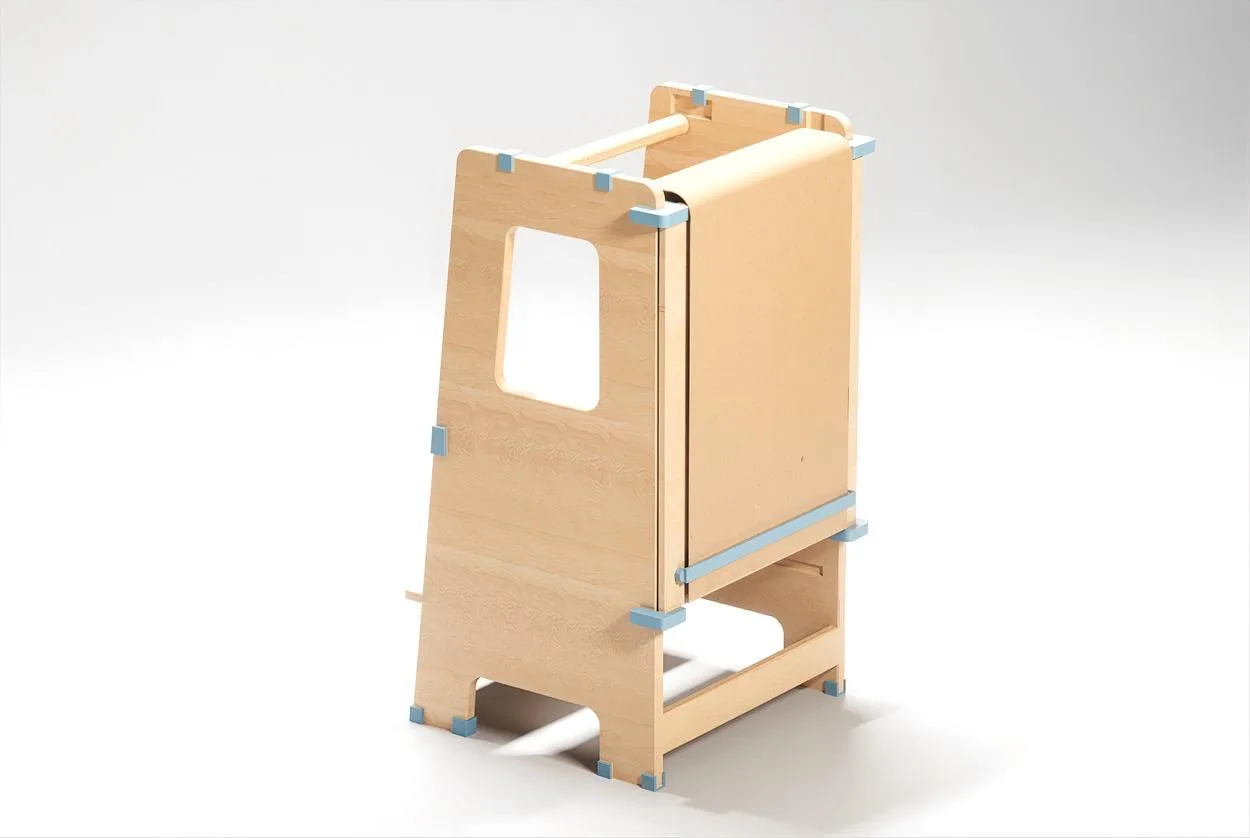Torre de Aprendizaje en madera clara vista de frente en ángulo, con ventana rectangular recortada en el panel lateral y peldaños en la base, sobre fondo blanco.